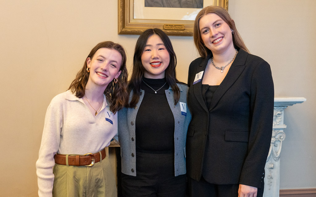 Three women standing together and smiling.